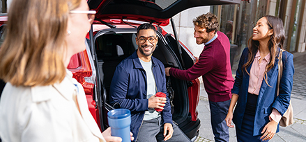 A group of four people chatting with coffee at an open car boot