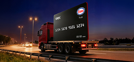 A truck driving at night carrying a scaled-up version of the Esso Card™ Truck behind it
